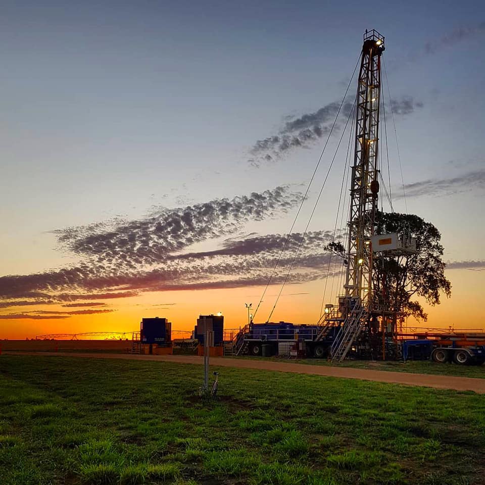 A picturesque sunset view of a well servicing rig, with the vibrant colors of the setting sun casting a warm glow on the equipment and surrounding landscape